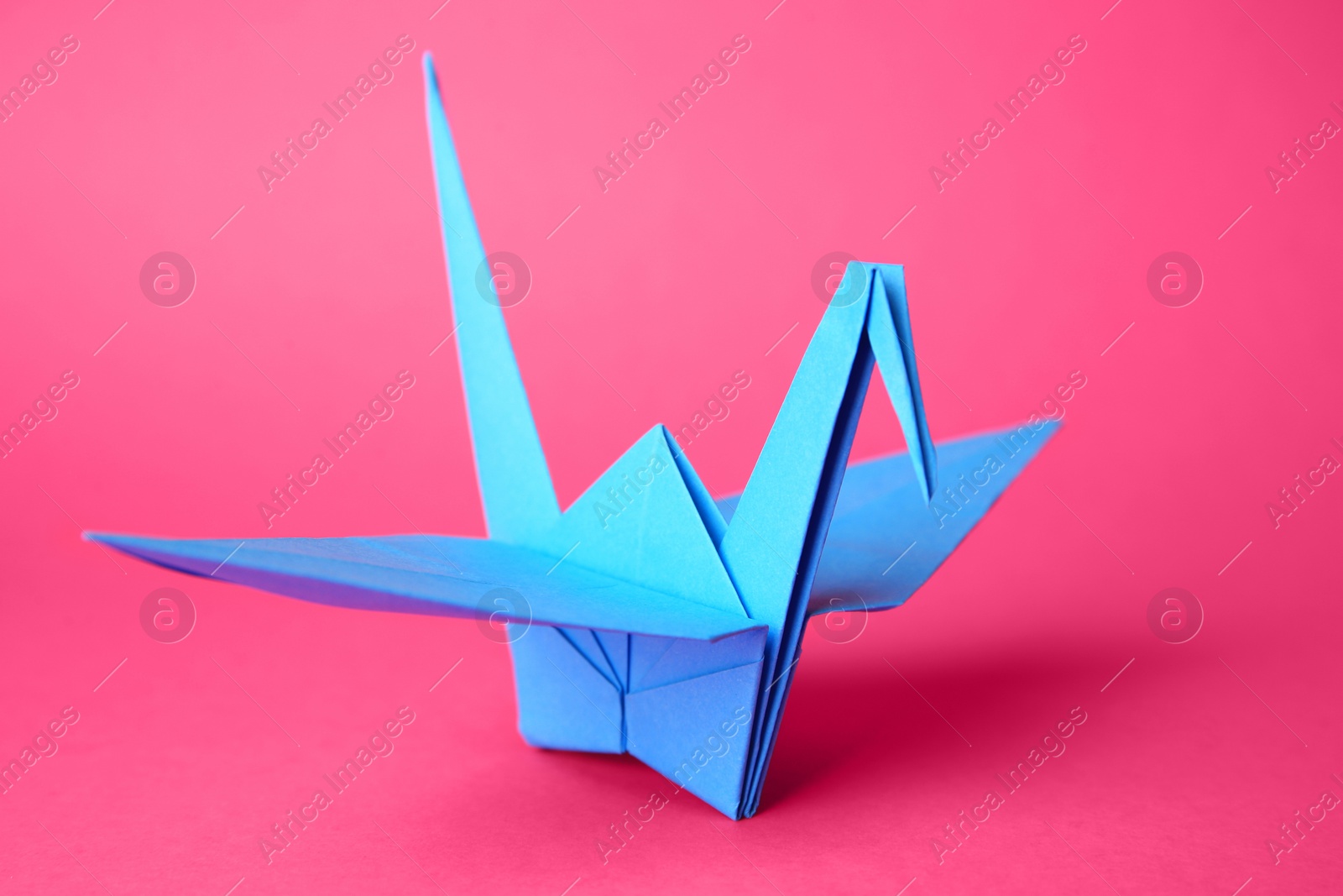 Photo of Origami art. Handmade paper crane on pink background, closeup