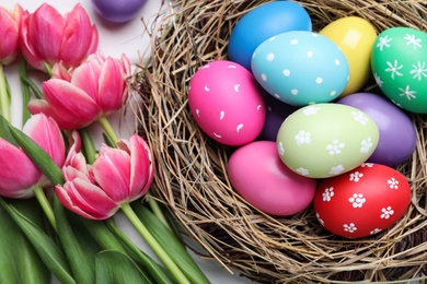 Colorful eggs in nest and tulips on white background, flat lay. Happy Easter