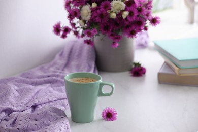 Photo of Cup of aromatic coffee, beautiful flowers and violet cloth on white table