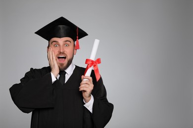 Photo of Emotional student with graduation hat and diploma on grey background. Space for text