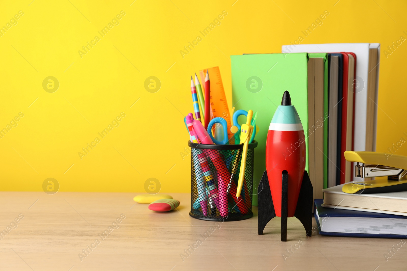 Photo of Bright toy rocket and school supplies on wooden table. Space for text