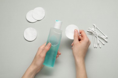 Woman holding makeup remover and cotton pad on light grey background, top view