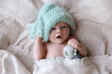 Cute newborn baby in warm hat with toy lying on bed, top view