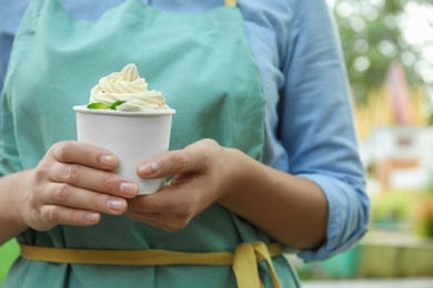 Photo of Woman holding cup with tasty frozen yogurt outdoors, closeup