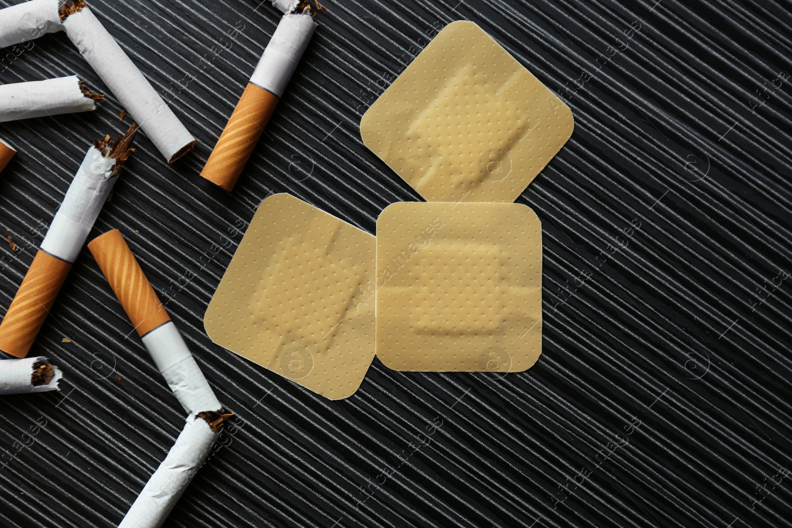 Photo of Nicotine patches and broken cigarettes on black table, flat lay