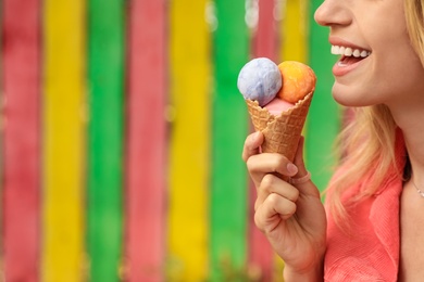 Photo of Happy young woman with delicious ice cream in waffle cone outdoors, closeup. Space for text