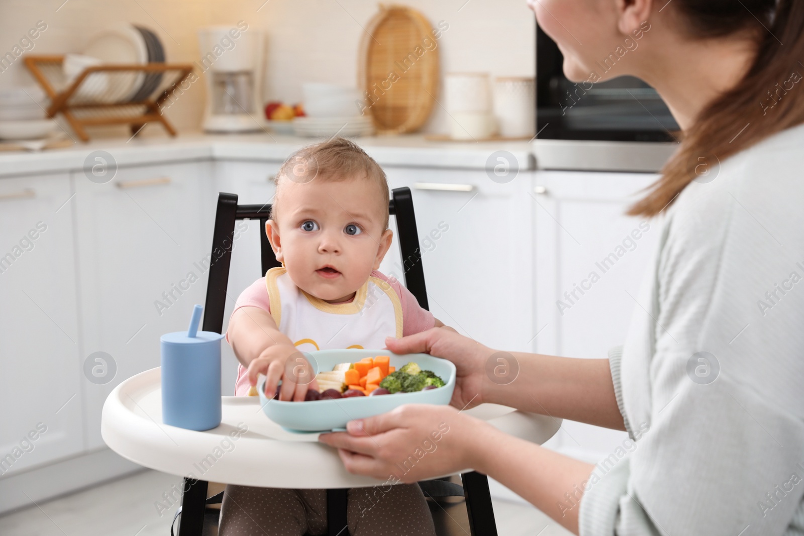 Photo of Mother feeding her cute little baby in kitchen