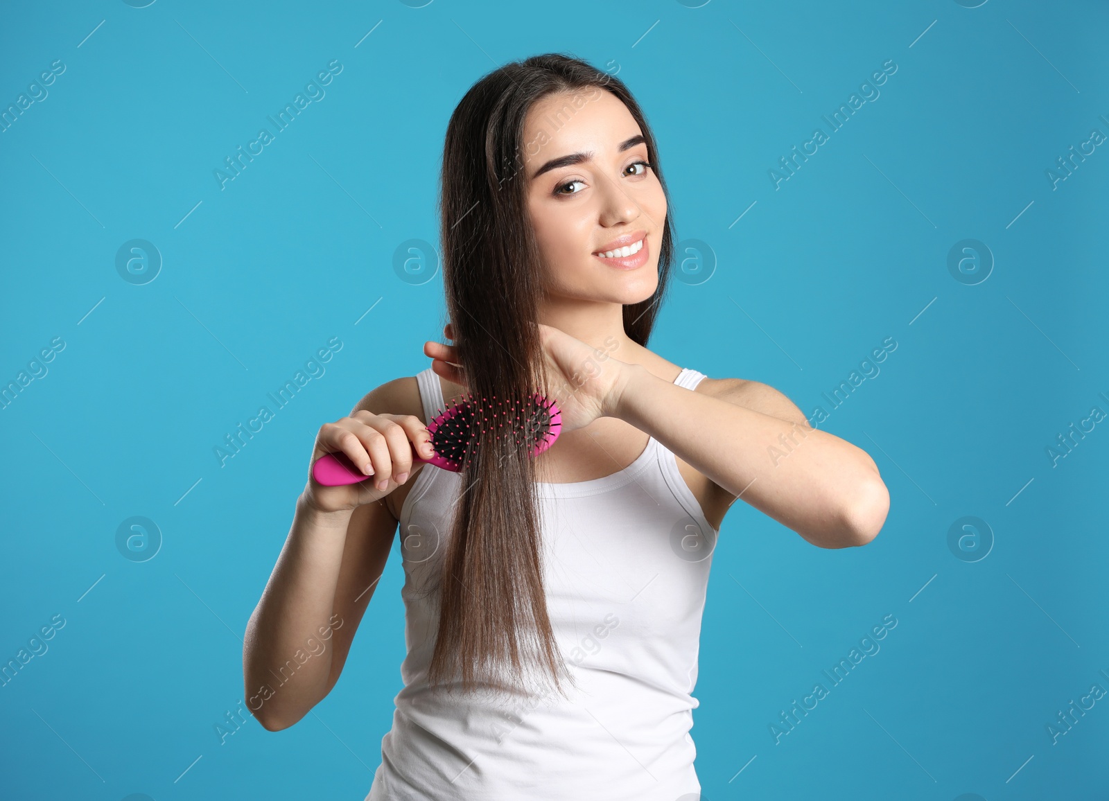 Photo of Beautiful smiling young woman with hair brush on color background