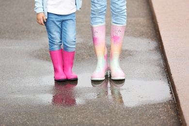 Mother and daughter wearing rubber boots on street, closeup