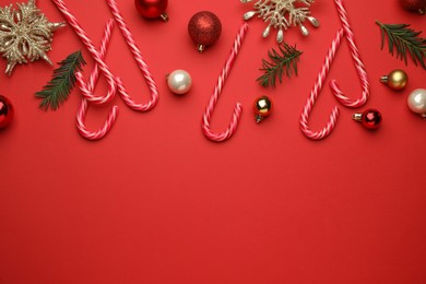 Flat lay composition with sweet candy canes and Christmas decor on red background, space for text
