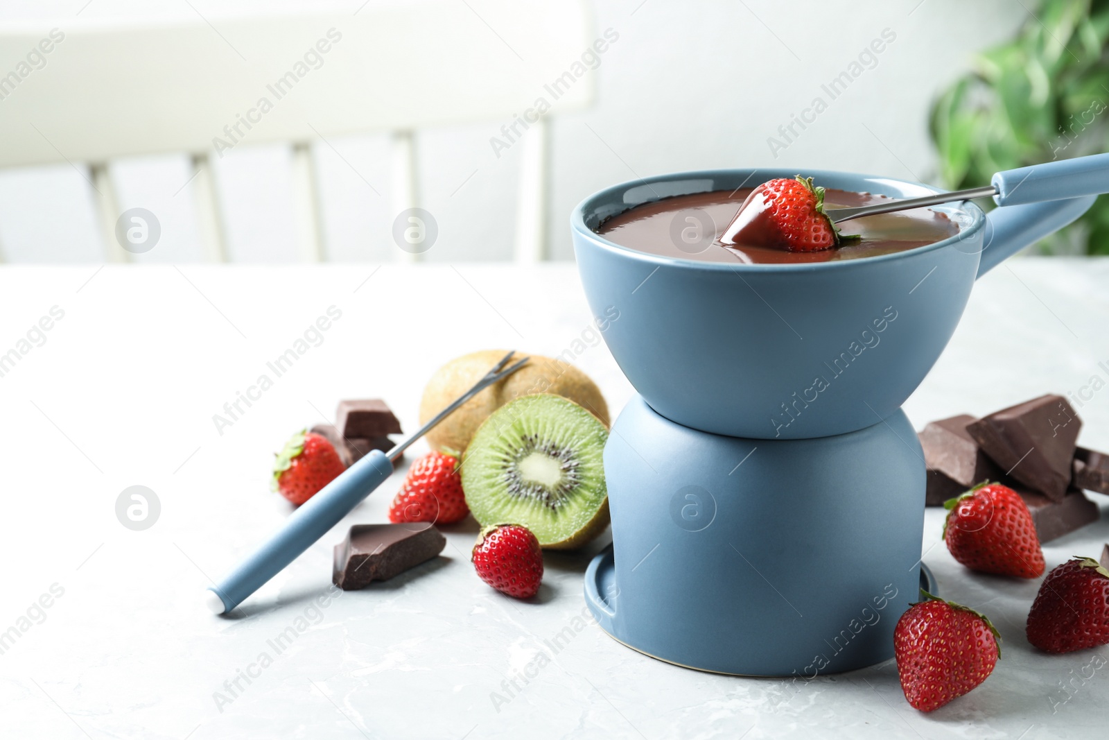 Photo of Dipping strawberry into fondue pot with chocolate on light marble table