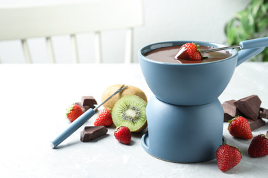 Photo of Dipping strawberry into fondue pot with chocolate on light marble table