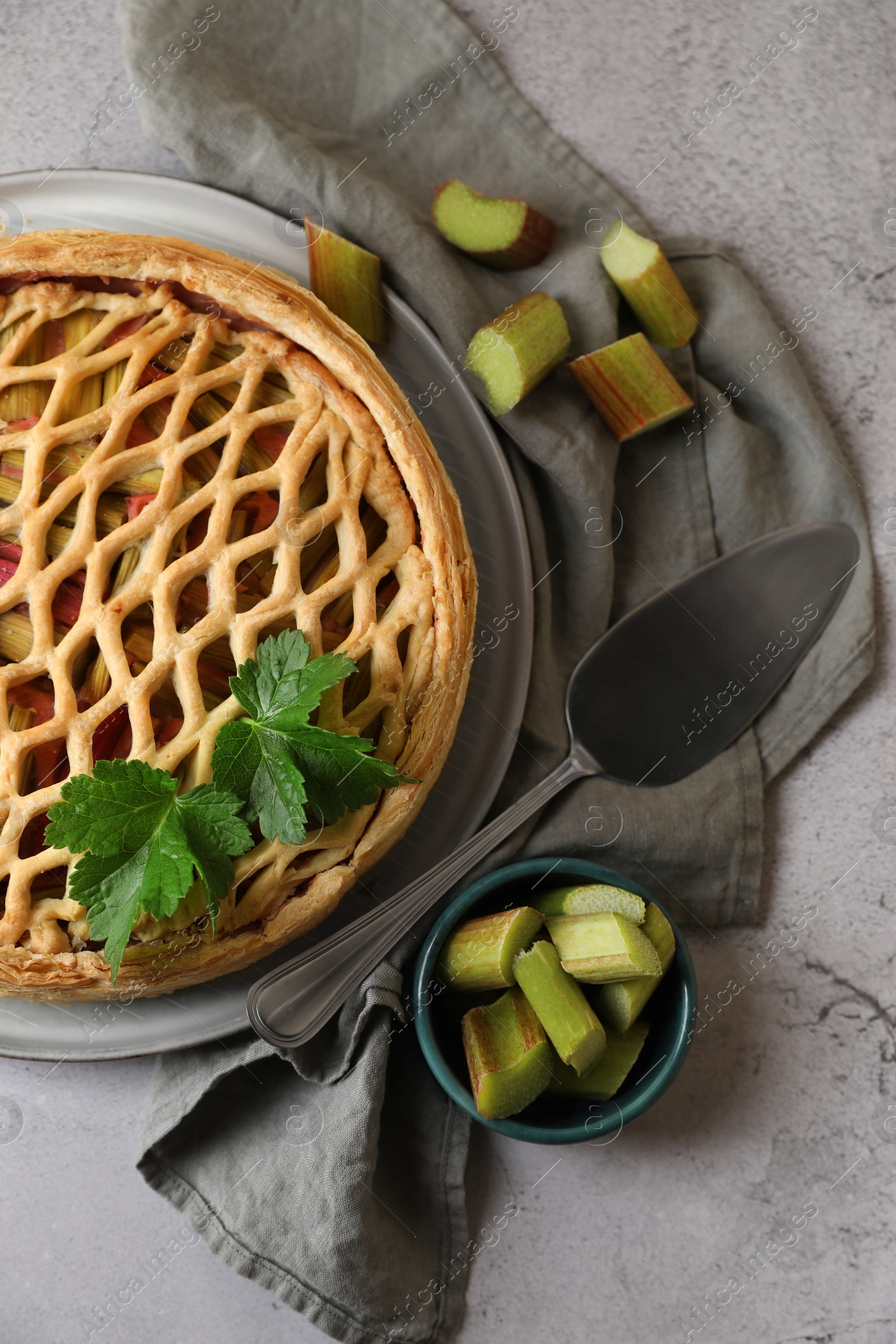 Photo of Freshly baked rhubarb pie, cut stalks and cake server on light grey table, flat lay