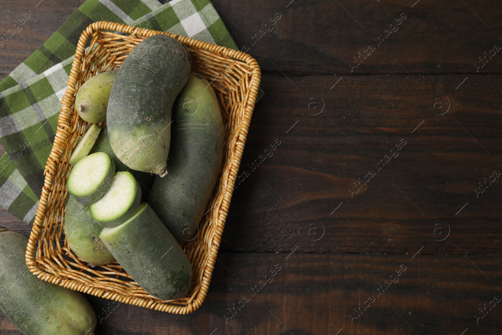 Photo of Green daikon radishes in wicker basket on wooden table, top view. Space for text