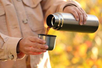 Photo of Woman pouring tea from thermos into cup lid outdoors, closeup