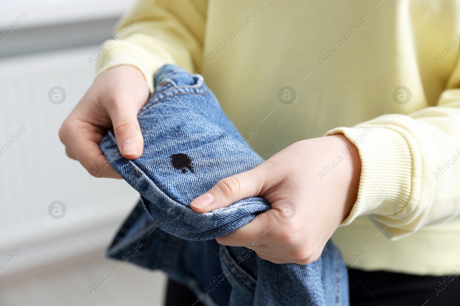 Photo of Woman holding jeans with black ink stain on blurred background, closeup