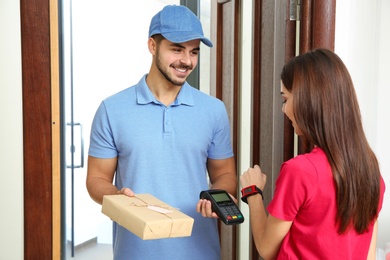 Photo of Woman with smartwatch using terminal for delivery payment indoors