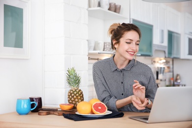 Photo of Young blogger with fruits and laptop on kitchen