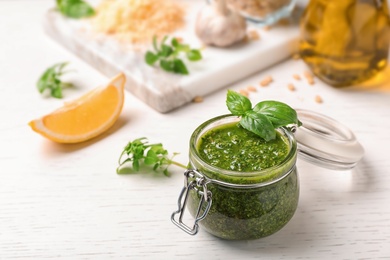 Composition with homemade basil pesto sauce in glass jar on table