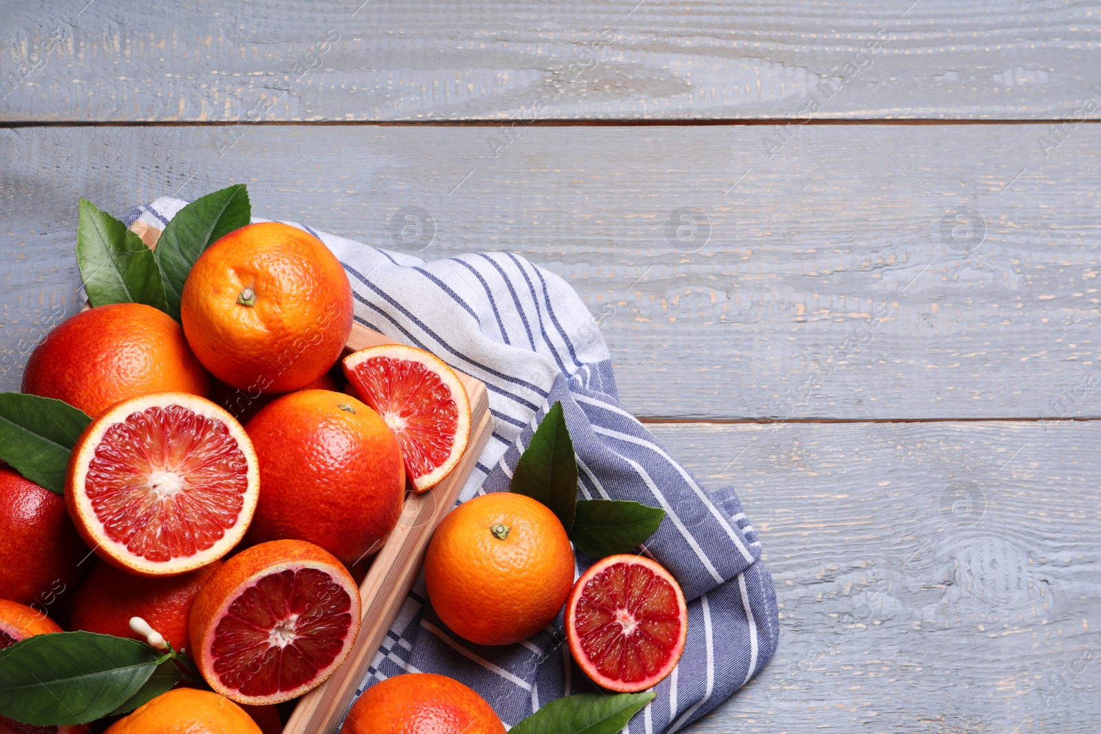 Photo of Crate of ripe red oranges and green leaves on grey wooden table, flat lay. Space for text