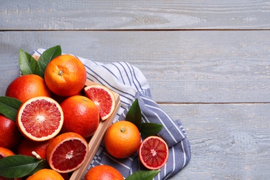 Photo of Crate of ripe red oranges and green leaves on grey wooden table, flat lay. Space for text