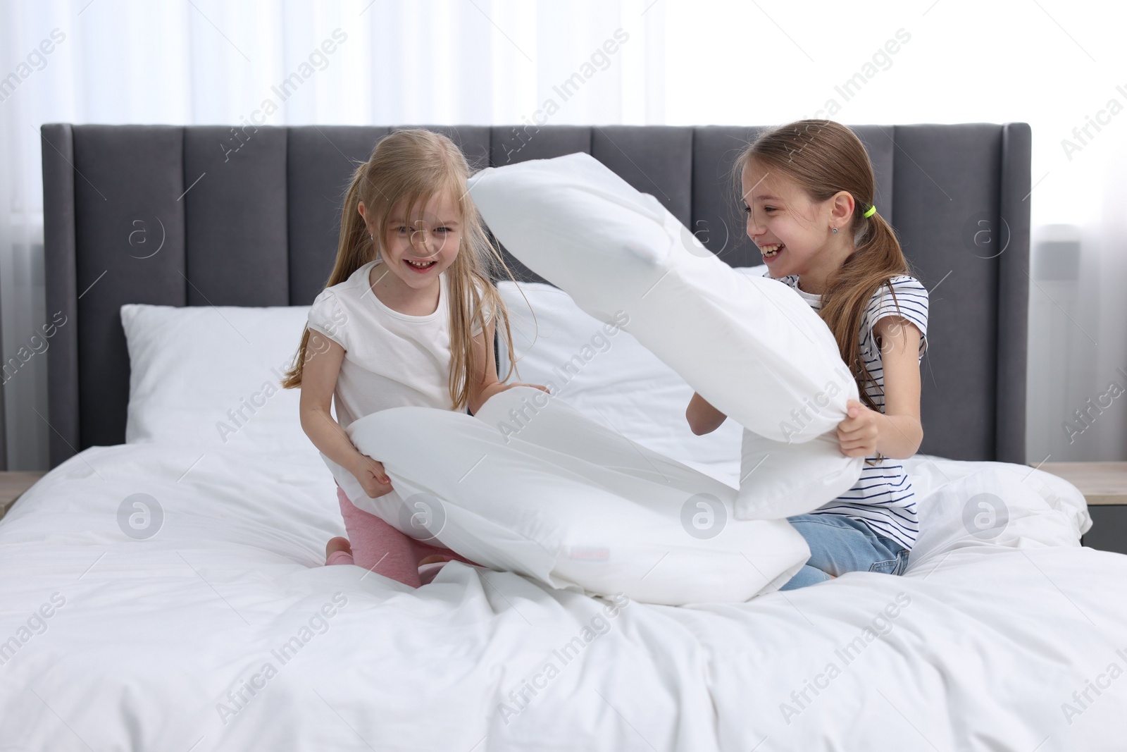 Photo of Cute little sisters having pillow fight on bed at home