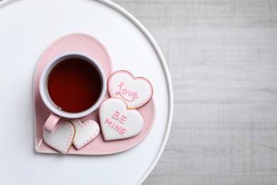 Photo of Delicious heart shaped cookies and cup of tea on white table, top view. Space for text