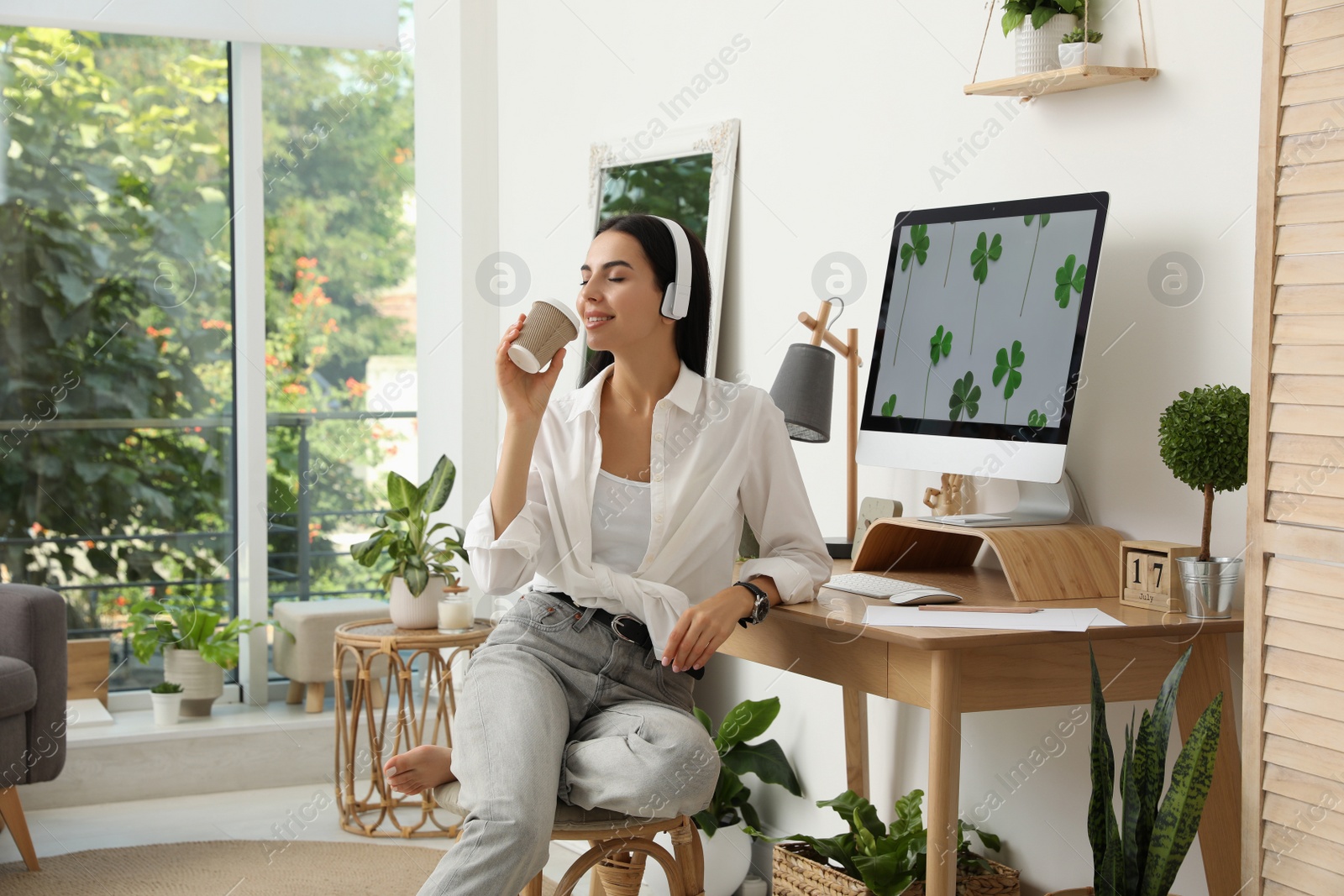 Photo of Young woman with cup of drink at table in room. Home office