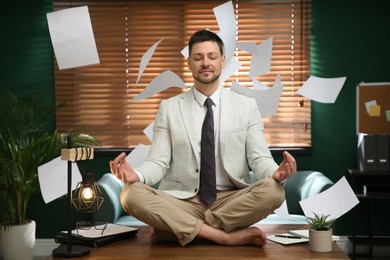 Photo of Calm businessman meditating on office desk in middle of busy work day