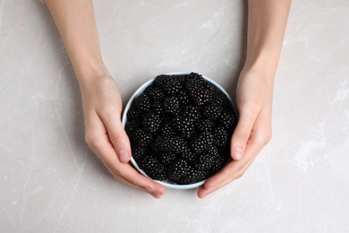 Photo of Woman with bowl of blackberries at marble table, top view