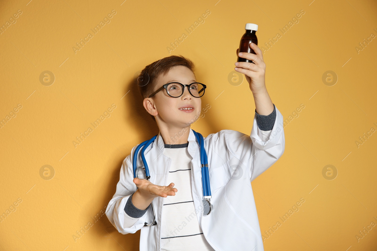 Photo of Cute little child in doctor coat with medication on color background