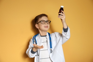 Photo of Cute little child in doctor coat with medication on color background