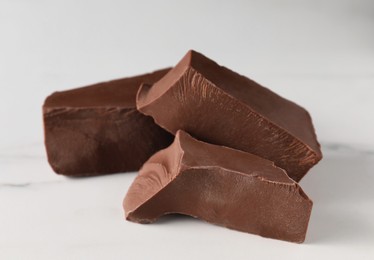 Pieces of tasty milk chocolate on white table, closeup