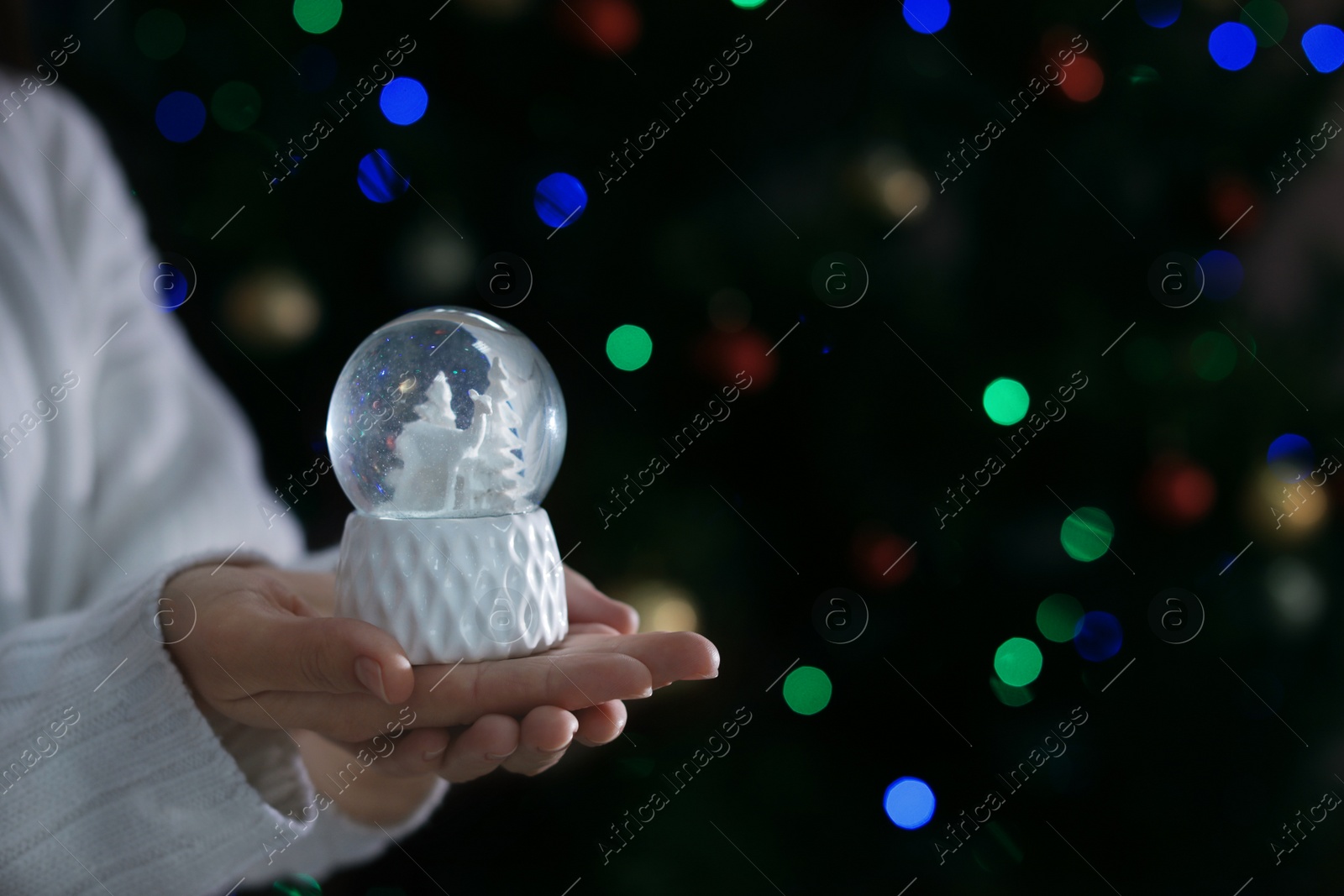 Photo of Woman holding snow globe on blurred background, closeup. Space for text