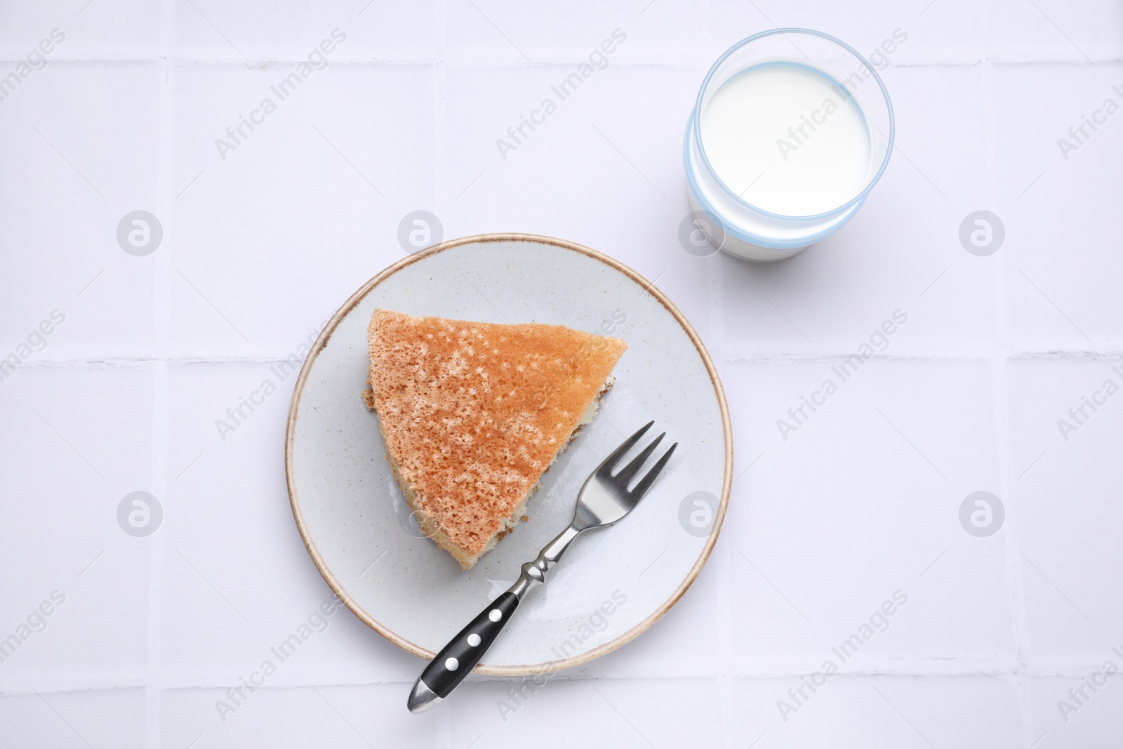 Photo of Piece of tasty sponge cake served with milk on white tiled table, flat lay