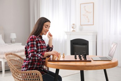 Young woman playing chess with partner through online video chat at home