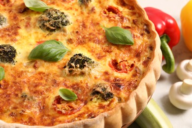 Photo of Delicious homemade vegetable quiche and basil leaves on table, closeup