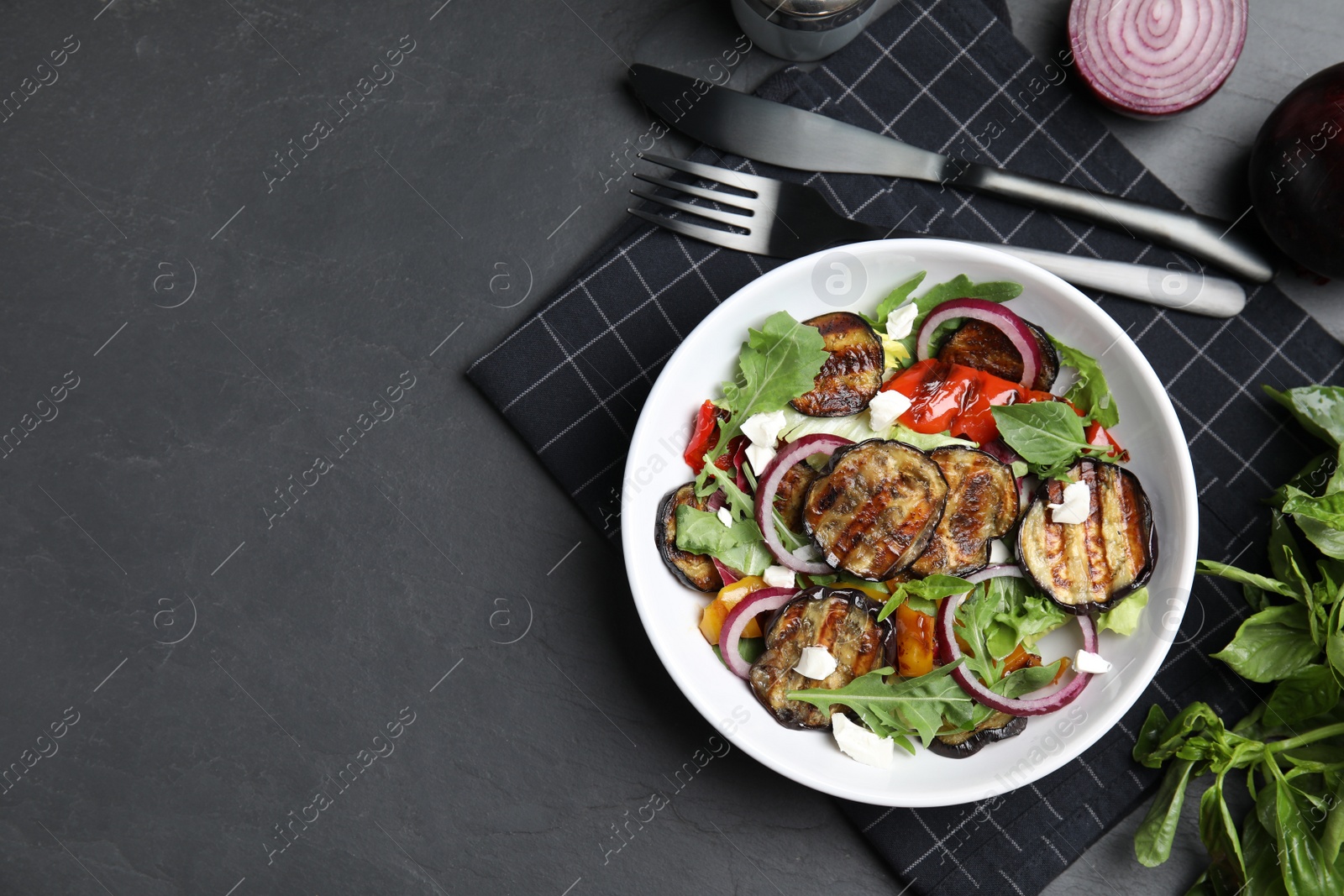 Photo of Delicious salad with roasted eggplant, cheese and arugula served on black table, flat lay. Space for text