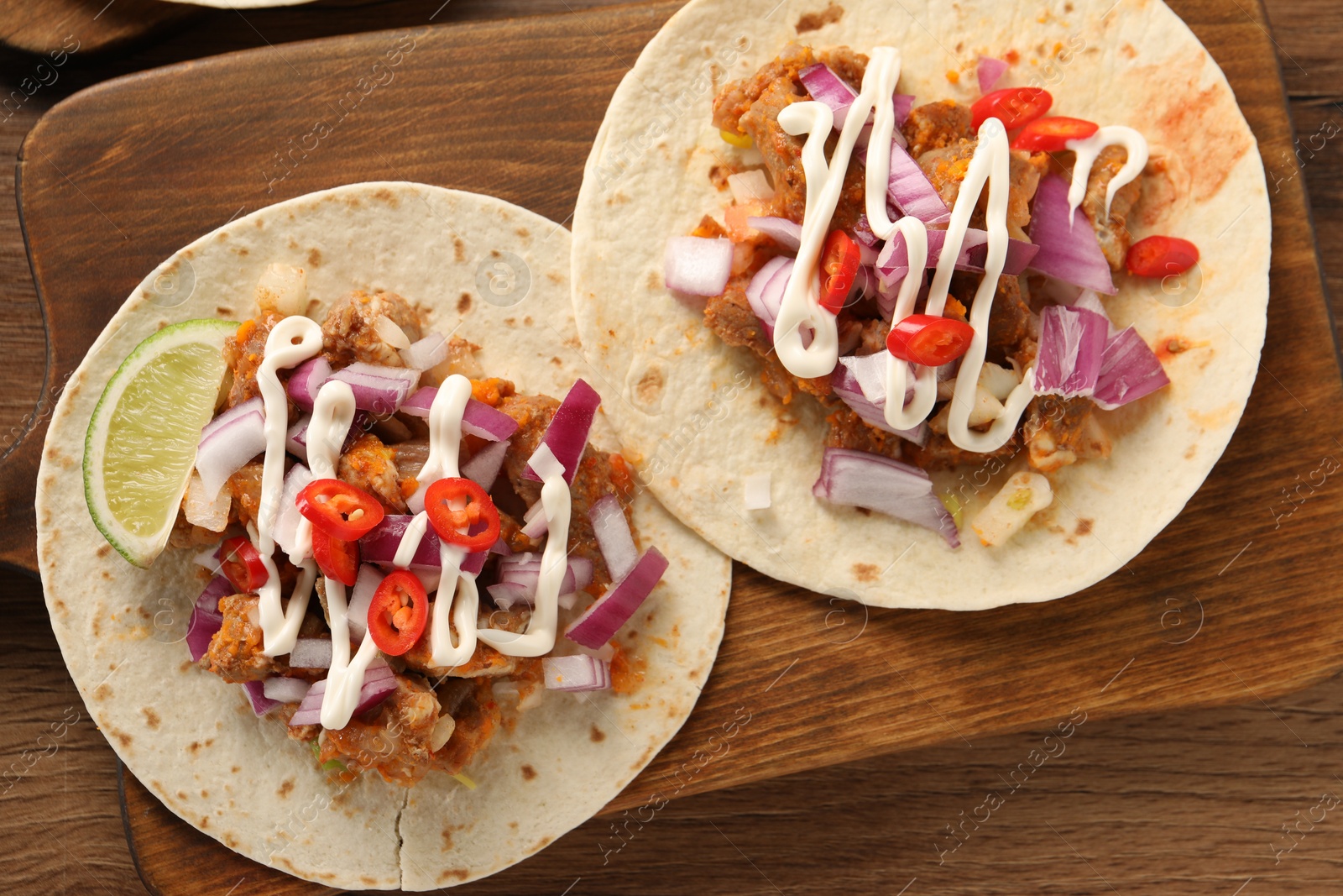 Photo of Delicious tacos with vegetables, meat and sauce on wooden table, top view