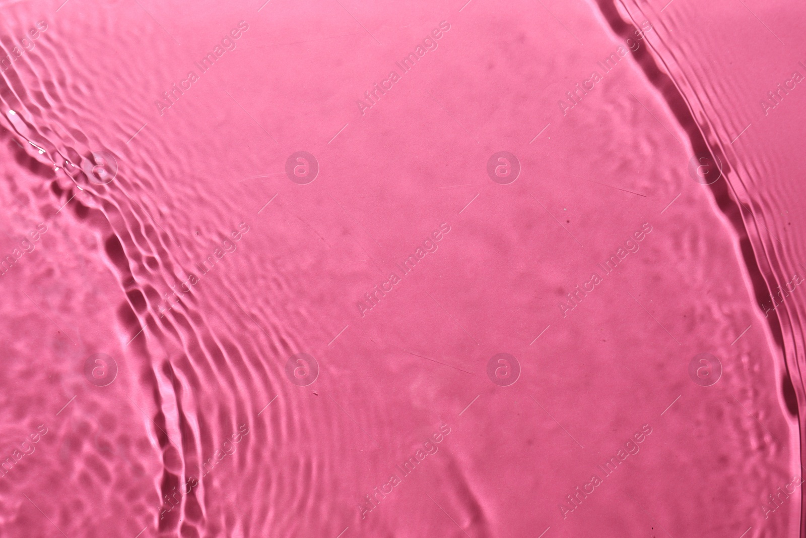 Photo of Rippled surface of clear water on bright pink background, top view