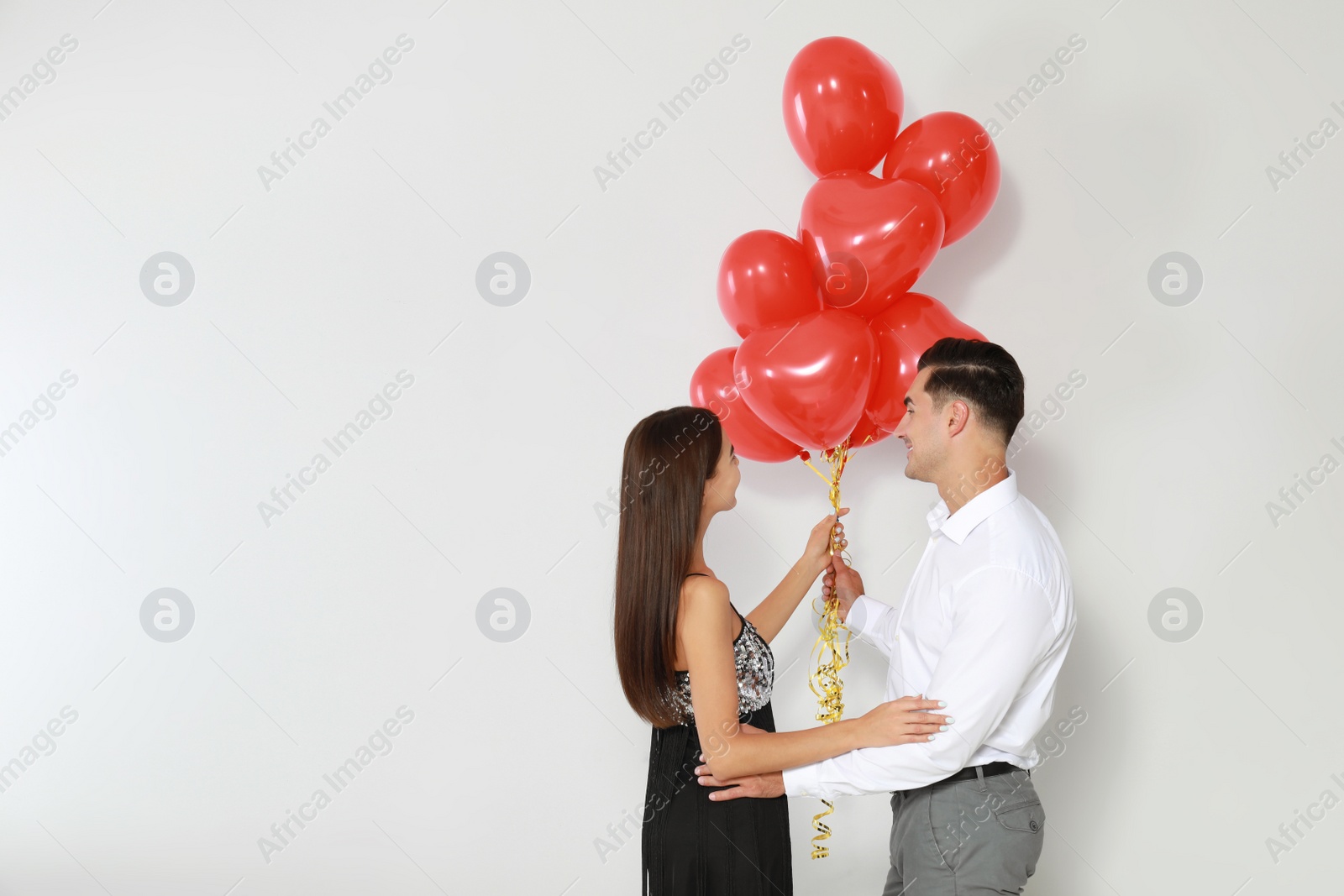 Photo of Beautiful couple with heart shaped balloons on light background, space for text