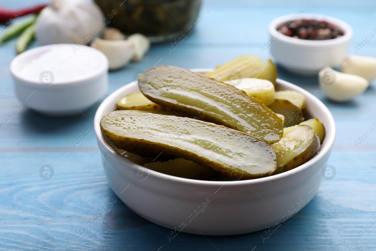 Photo of Bowl with pickled cucumbers on light blue table, closeup