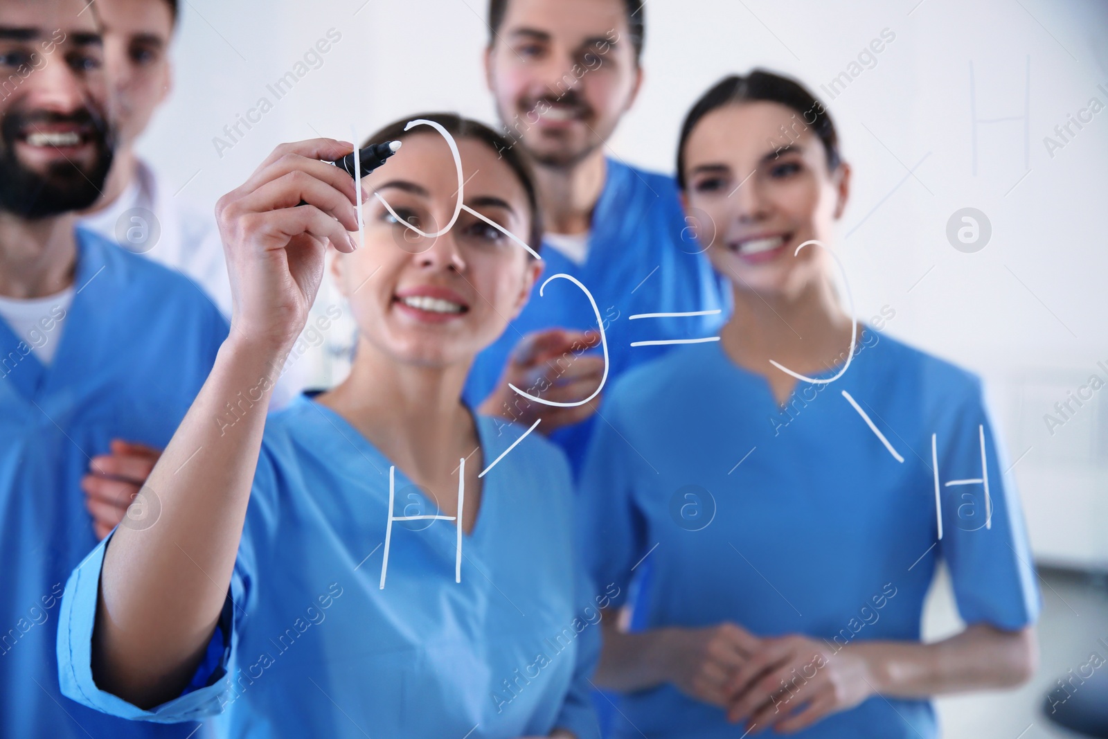 Photo of Medical students writing chemical formula on glass whiteboard in laboratory