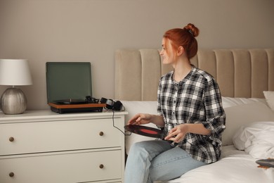 Photo of Young woman using turntable in bedroom at home