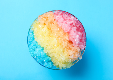 Rainbow shaving ice in glass dessert bowl on light blue background, top view