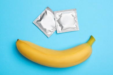 Photo of Condoms with banana on light blue background, flat lay. Safe sex