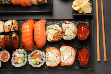 Photo of Delicious sushi rolls and chopsticks on black table, flat lay