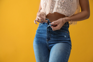 Photo of Woman unbuttoning jeans on yellow background, closeup