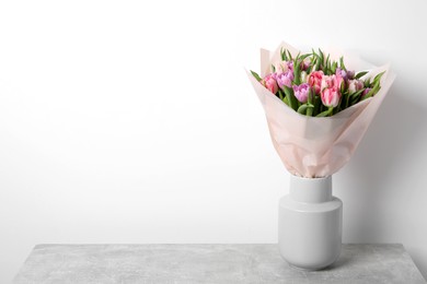 Vase with bouquet of beautiful tulips on grey table. Space for text