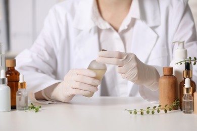 Dermatologist with bottle of cosmetic product at white table indoors, closeup. Development and testing